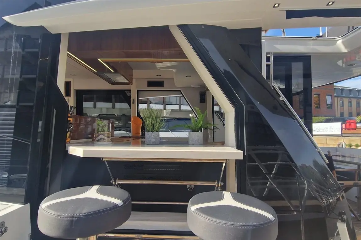 Sleek yacht kitchenette with bar stools, indoor plants, and modern lighting, featuring a stylish countertop and appliances.